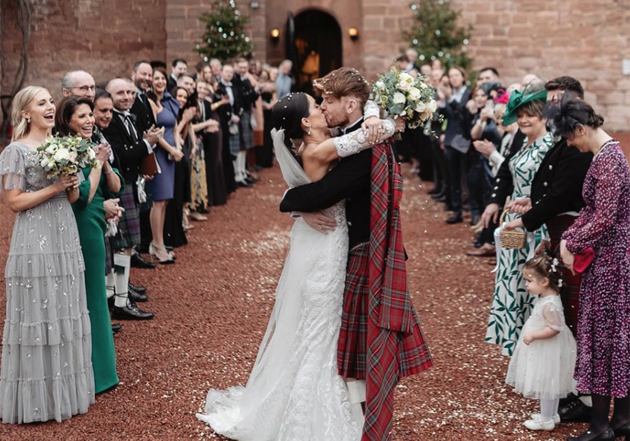 Bride and groom kiss outside castle with their guests in background